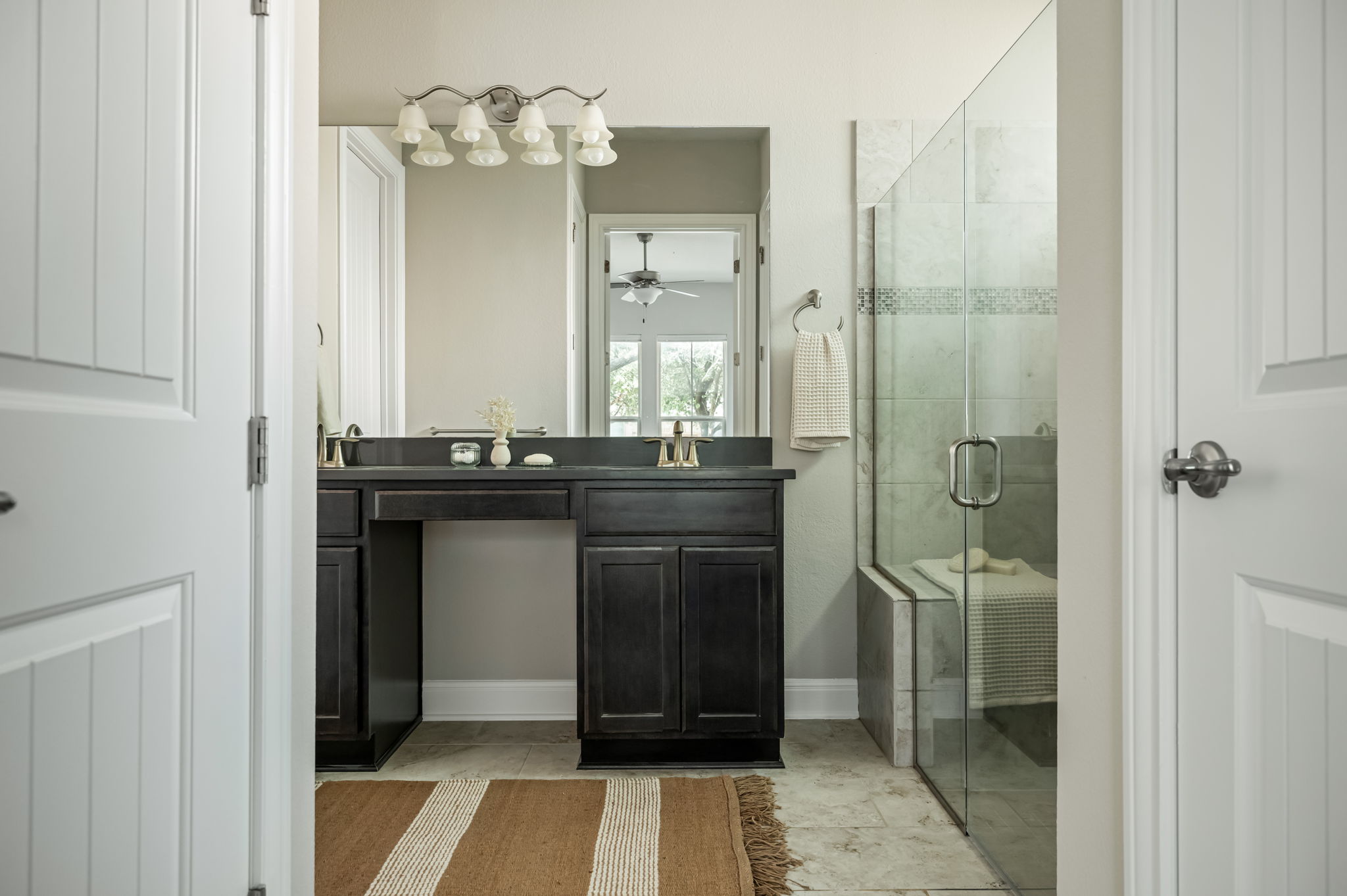 2516 Hopsack Mills Road Austin, TX 78748 - Photo 21 of 39 Double vanity with dark wood cabinetry and integrated sinks, large mirrored wall, glass-enclosed shower with tile surround and integrated bench, and tiled flooring