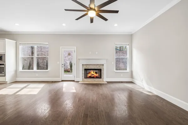 an empty room with windows a fireplace a ceiling fan and wooden floor