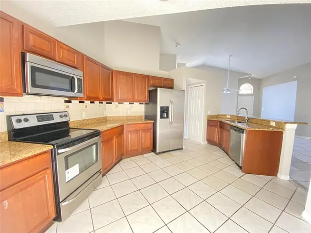 a kitchen with stainless steel appliances a stove a microwave a sink a refrigerator white cabinets and black chairs