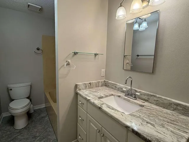 a bathroom with a granite countertop sink a toilet and a mirror