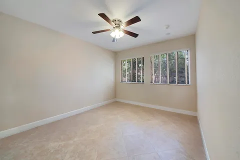an empty room with ceiling fan and windows