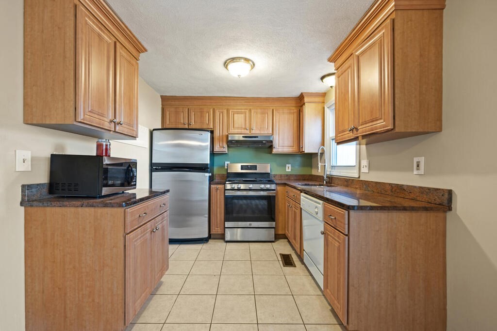 802 Lawrence Street, Unit D Lowell, MA 01852 - Photo 15 of 26 a kitchen with stainless steel appliances granite countertop a stove top oven a sink and dishwasher a refrigerator with wooden cabinets