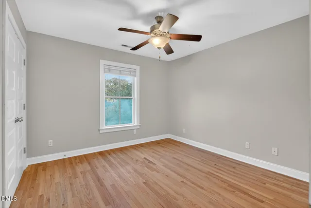 an empty room with wooden floor chandelier fan and windows