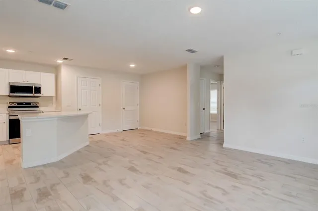 a view of an empty room with kitchen and window