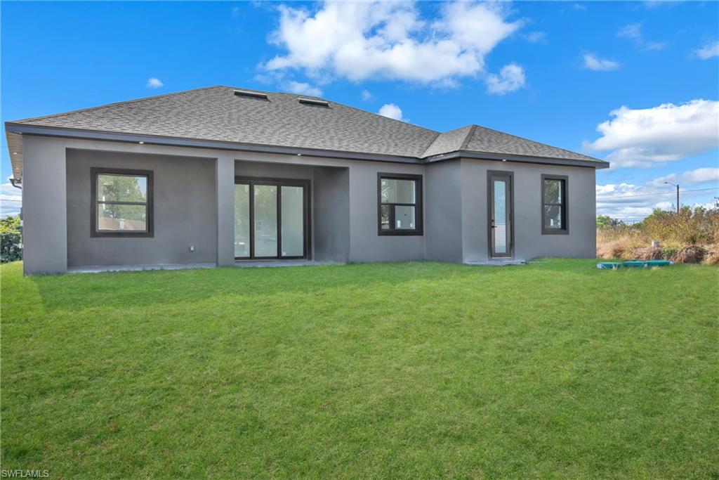 3110 23rd Street Southwest Lehigh Acres, FL 33976 - Photo 27 of 27 Rear view of house featuring a yard, stucco siding, a shingled roof, and a patio