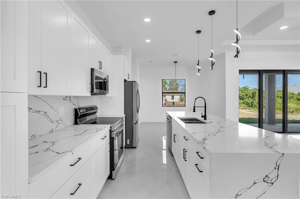 3110 23rd Street Southwest Lehigh Acres, FL 33976 - Photo 3 of 27 Kitchen with stainless steel appliances, light stone countertops, a large island, hanging light fixtures, and white cabinetry