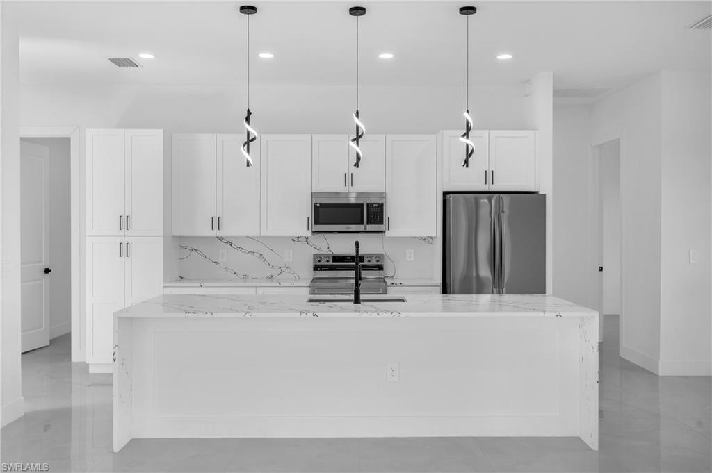 3110 23rd Street Southwest Lehigh Acres, FL 33976 - Photo 4 of 27 Kitchen with light stone countertops, white cabinets, and stainless steel appliances