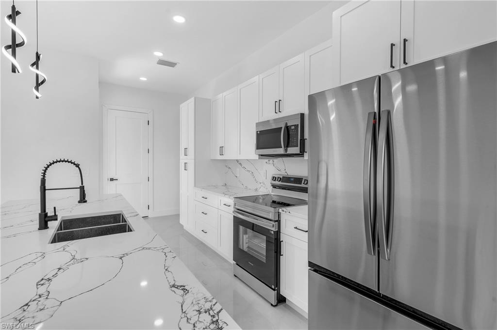 3110 23rd Street Southwest Lehigh Acres, FL 33976 - Photo 5 of 27 Kitchen featuring stainless steel appliances, white cabinetry, light stone countertops, and pendant lighting
