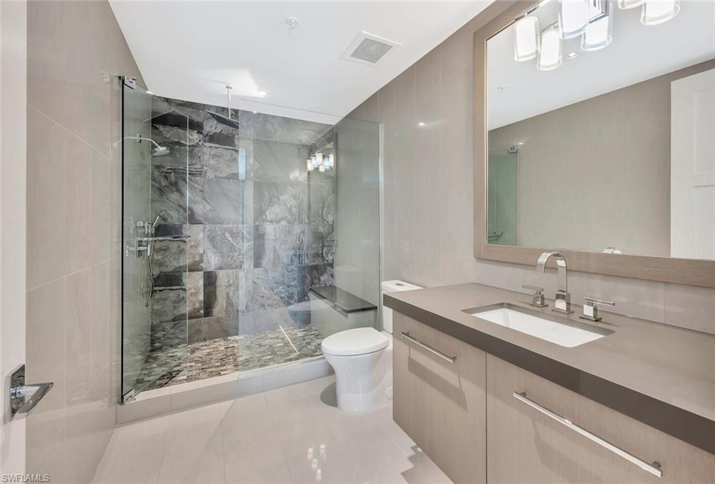 490 5th Street South, Unit 101 Naples, FL 34102 - Photo 31 of 50 a bathroom with a granite countertop sink a toilet a mirror and shower