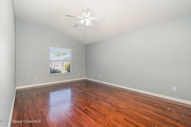 an empty room with wooden floor chandelier fan and windows