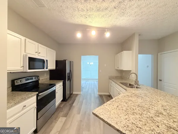 a kitchen with stainless steel appliances kitchen island granite countertop a stove top oven a sink dishwasher a refrigerator and cabinets with wooden floor