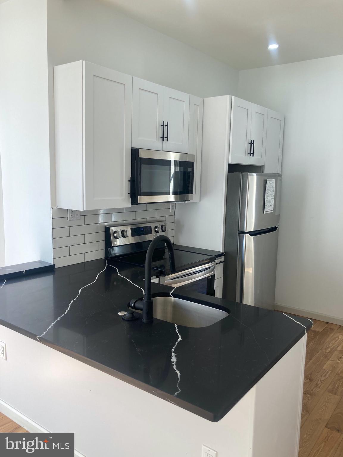 1901 West Diamond Street, Unit 2 Philadelphia, PA 19121 - Photo 4 of 9 a kitchen with a sink a microwave a refrigerator and white cabinets