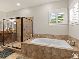 514 North Olympic Way Midway, UT 84049 - Photo 12 of 30 Spacious bathroom featuring a built-in jetted tub with stone surround, a separate glass-enclosed shower, dual vanity with wood cabinetry, tile flooring, and plantation shutters on multiple windows