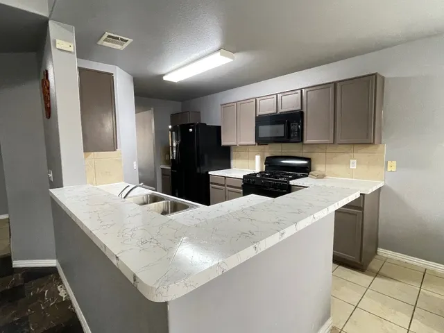 a kitchen with granite countertop a refrigerator a stove a sink a microwave and wooden cabinets