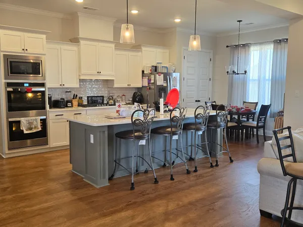 a kitchen with stainless steel appliances granite countertop a stove top oven a sink a dining table and chairs with wooden floor