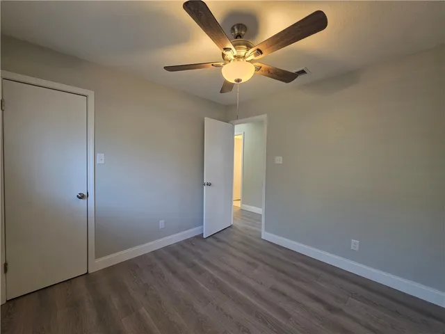 an empty room with wooden floor fan and windows