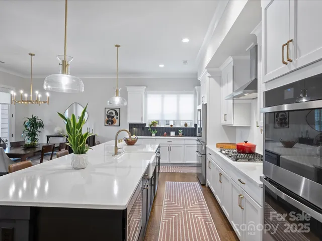 a kitchen with stainless steel appliances a sink dishwasher a microwave a stove and white cabinets with wooden floor