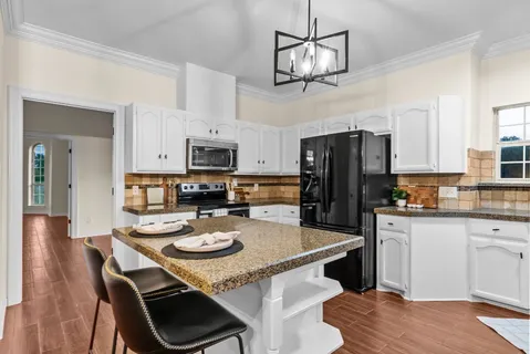 a kitchen with stainless steel appliances granite countertop a dining table chairs refrigerator and microwave