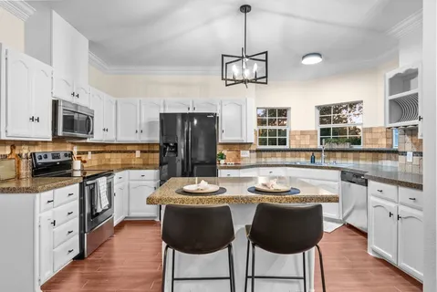 a kitchen with stainless steel appliances kitchen island granite countertop a dining table chairs and white cabinets