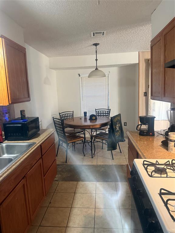 1117 Victoria Street Bellmead, TX 76705 - Photo 5 of 11 Kitchen featuring brown cabinets, decorative light fixtures, black microwave, white gas range oven, and light countertops