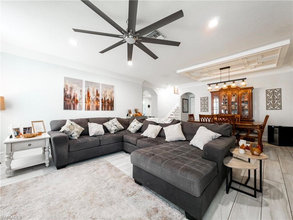 Living area with arched walkways, ceiling fan, crown molding, stairway, and recessed lighting