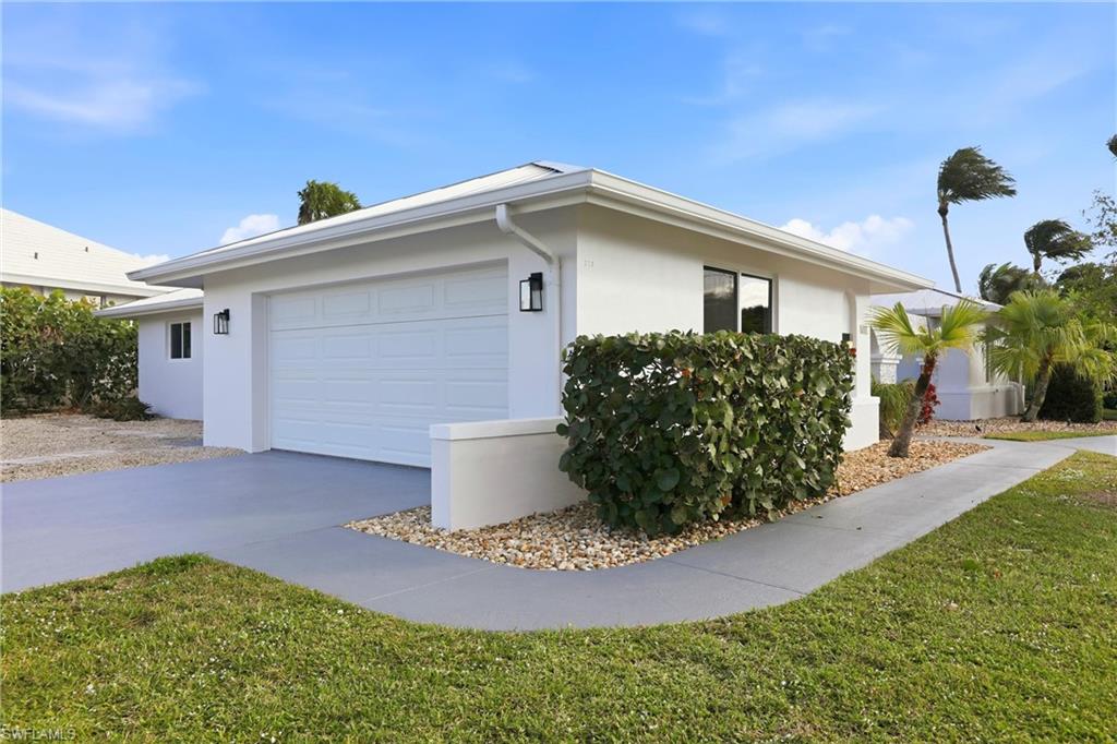 339 Landmark Street Marco Island, FL 34145 - Photo 2 of 50 View of side of property with concrete driveway, stucco siding, an attached garage, and a yard