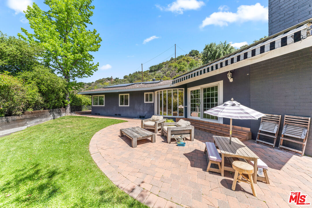 3940 Mandeville Canyon Road Los Angeles, CA 90049 - Photo 47 of 54 a patio with a table and chairs under an umbrella with a fire pit