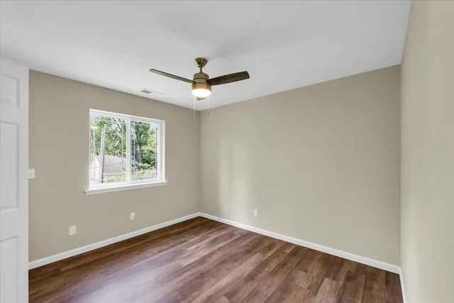 an empty room with wooden floor ceiling fan and windows