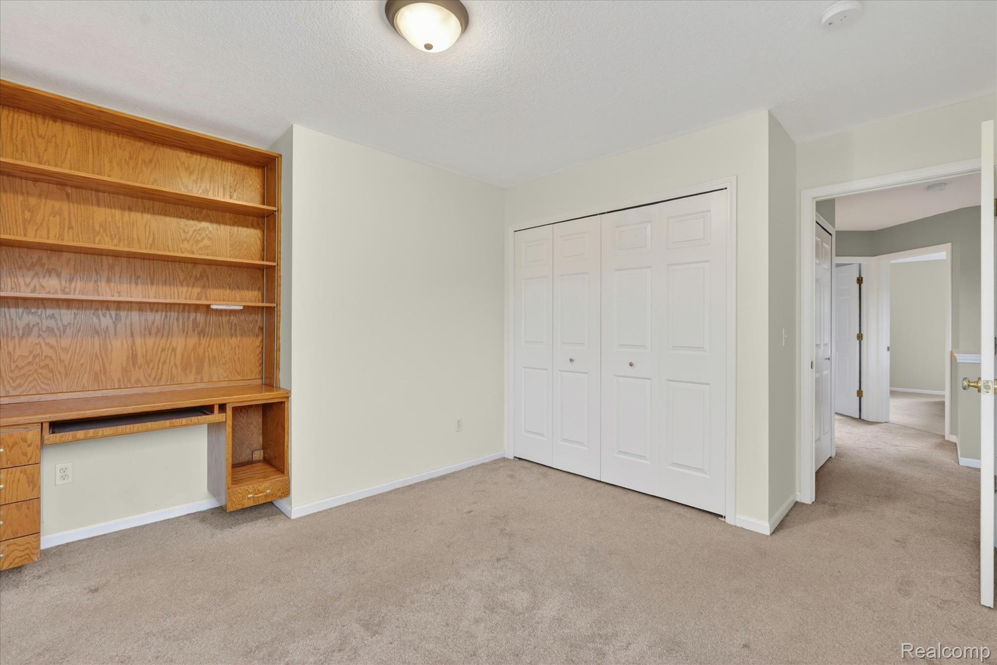 456 Lilly View Court Howell, MI 48843 - Photo 20 of 45 Room featuring a built-in wood-finish shelving unit with integrated desk space, a bi-fold closet, and neutral wall paint