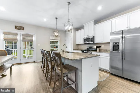 a kitchen with stainless steel appliances granite countertop a stove top oven a refrigerator a sink and white cabinets with wooden floor