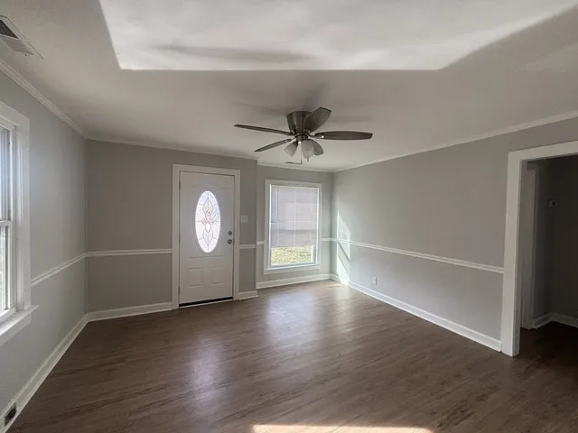 an empty room with wooden floor chandelier fan and windows