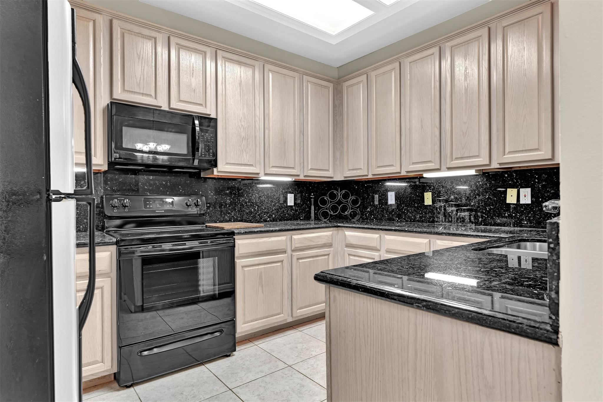 14420 Walters Road, Unit 16 Houston, TX 77014 - Photo 5 of 27 This kitchen features light wood cabinetry and sleek black granite countertops. It's equipped with modern black appliances, including a stove and microwave, and has a double sink. The space is well-lit with under-cabinet lighting and a bright ceiling fixture.
