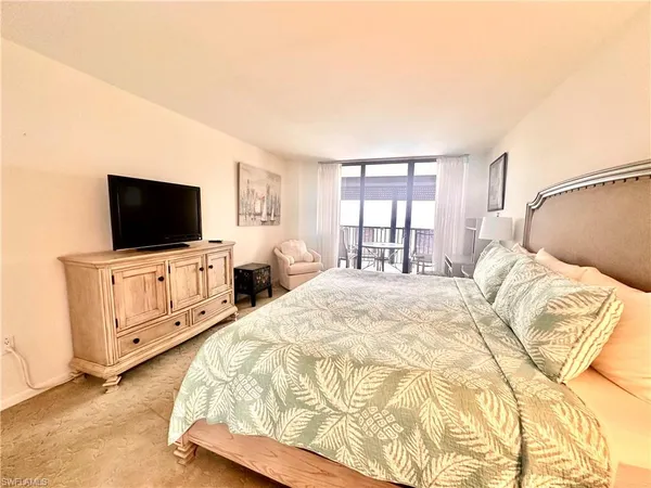 a bedroom with a flat screen tv on dresser and a window