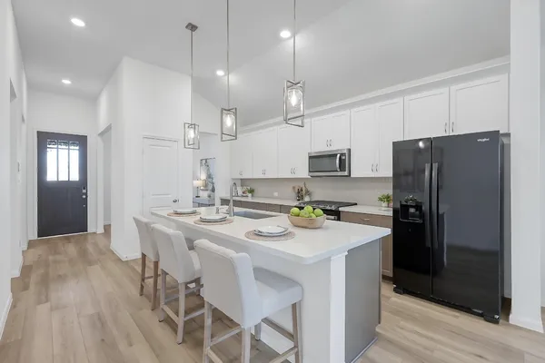 a kitchen with kitchen island granite countertop a refrigerator a sink a stove a dining table and chairs