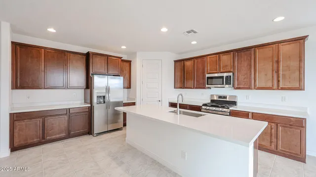 a large kitchen with stainless steel appliances granite countertop a stove a sink a refrigerator and white cabinets with wooden floor