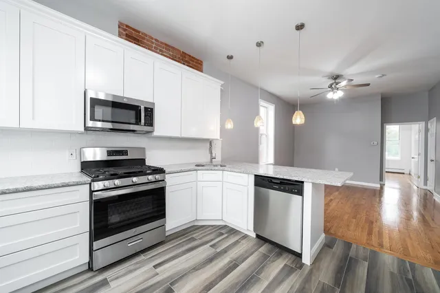 a kitchen with granite countertop a stove top oven a sink dishwasher a refrigerator and white cabinets with wooden floor