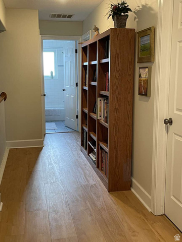 7030 West 2100 North Mendon, UT 84325 - Photo 32 of 67 Hallway featuring wood-finish flooring, built-in shelving, white baseboards, and a doorway leading to a tiled bathroom