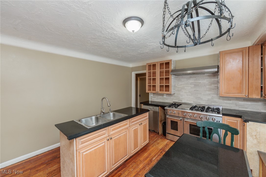5062 Lee Road Maple Heights, OH 44137 - Photo 11 of 50 Kitchen with dark countertops, stainless steel appliances, wall chimney exhaust hood, a center island with sink, and light wood-style floors