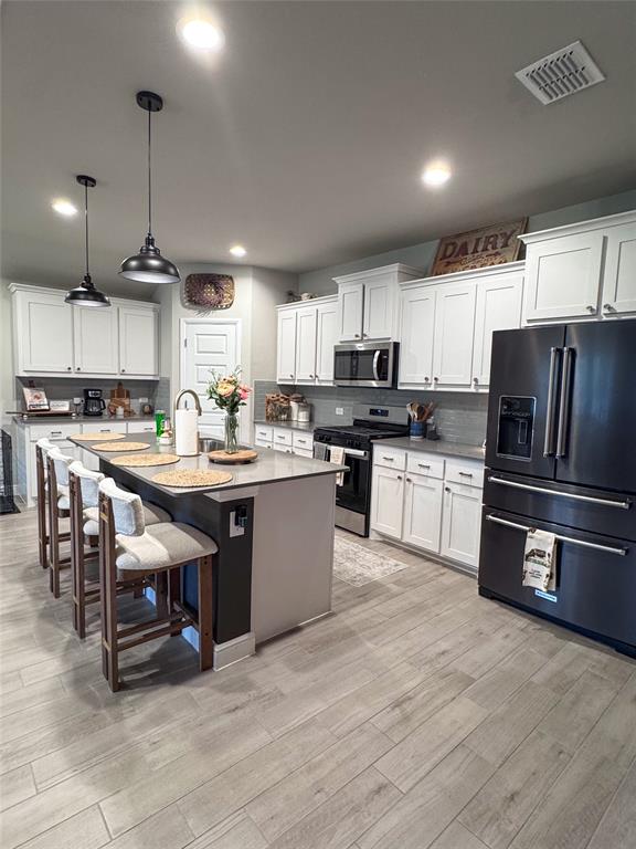 1908 Cookes Lane Cleburne, TX 76033 - Photo 3 of 17 Kitchen featuring a large central island with seating, pendant lighting, white cabinetry, dark-finish appliances, and wood-finish tile flooring