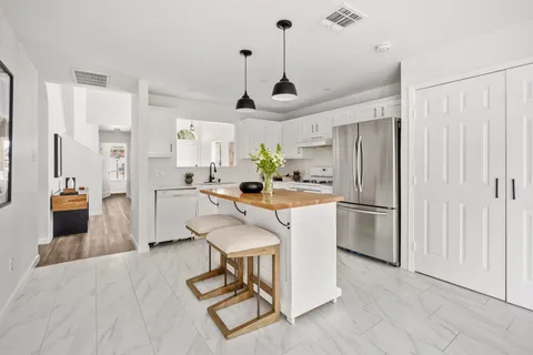 a kitchen with stainless steel appliances a refrigerator a stove a sink dishwasher and white cabinets with wooden floor