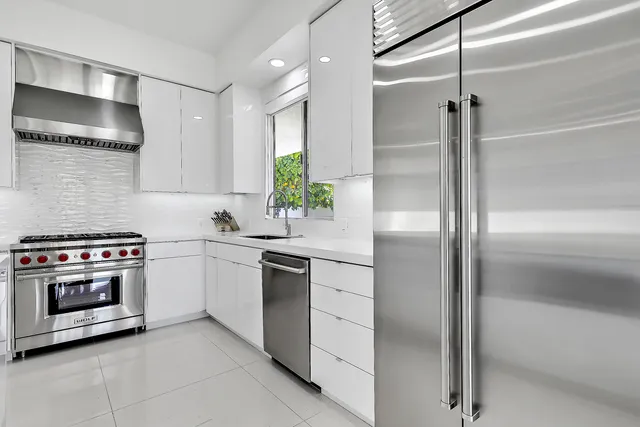 a kitchen with stainless steel appliances kitchen island granite countertop a refrigerator a sink a stove and a dining table with wooden floor