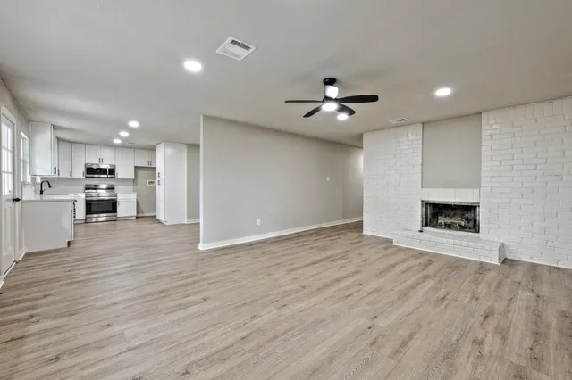 a view of an empty room with wooden floor and a kitchen