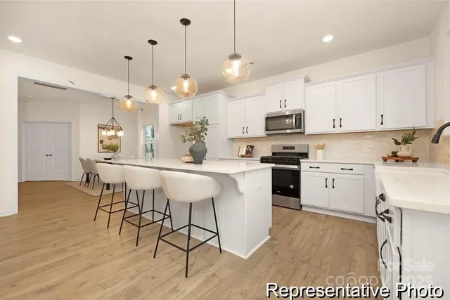a kitchen with stainless steel appliances granite countertop a stove a sink a microwave a refrigerator a stove and white cabinets with wooden floor