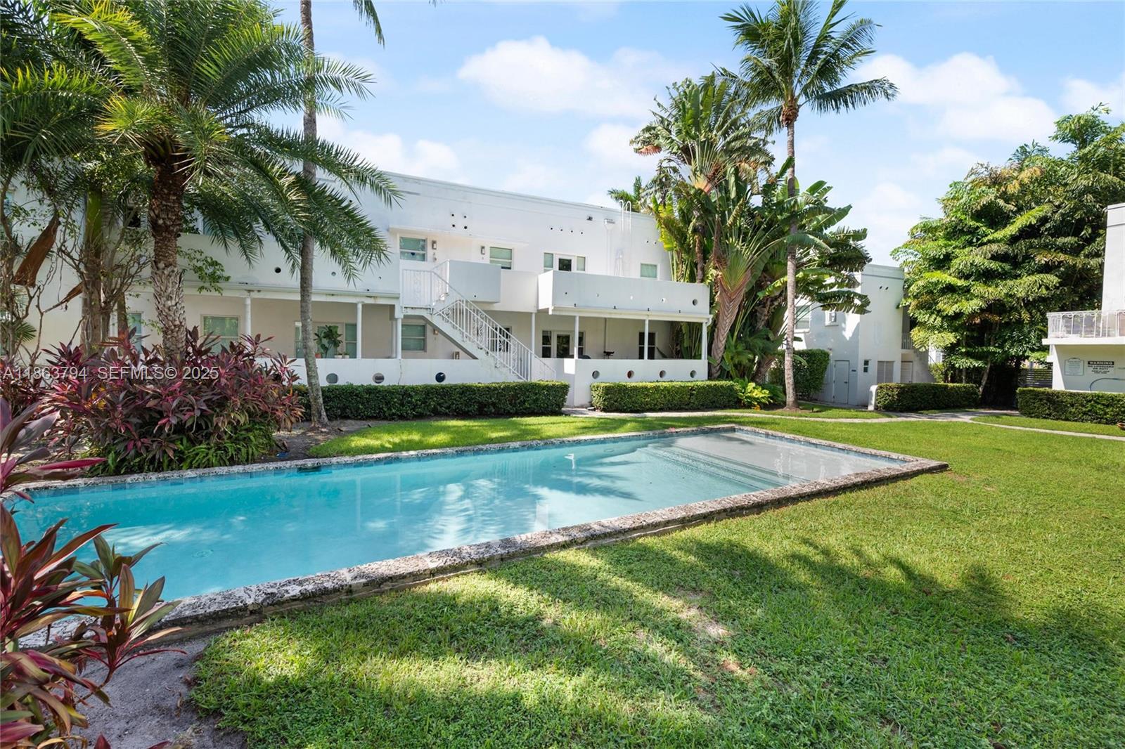 4015 Meridian Avenue, Unit 4 Miami Beach, FL 33140 - Photo 24 of 25 a view of a white house with a swimming pool and lawn chairs under palm trees