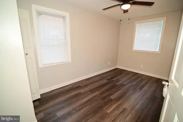 an empty room with wooden floor fan and windows