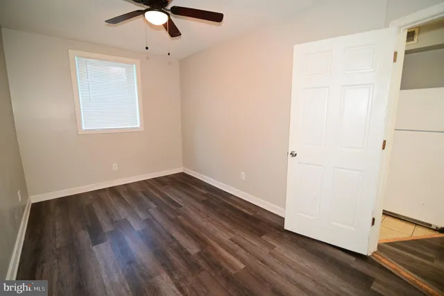 an empty room with wooden floor chandelier fan and windows
