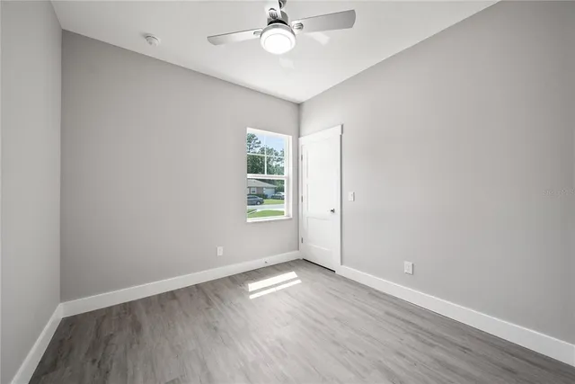 an empty room with wooden floor chandelier fan and windows