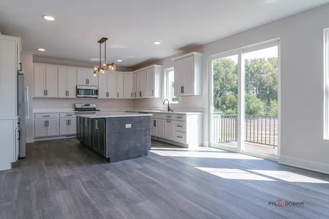 a kitchen with stainless steel appliances granite countertop a stove a sink dishwasher a refrigerator white cabinets and wooden floor next to a window