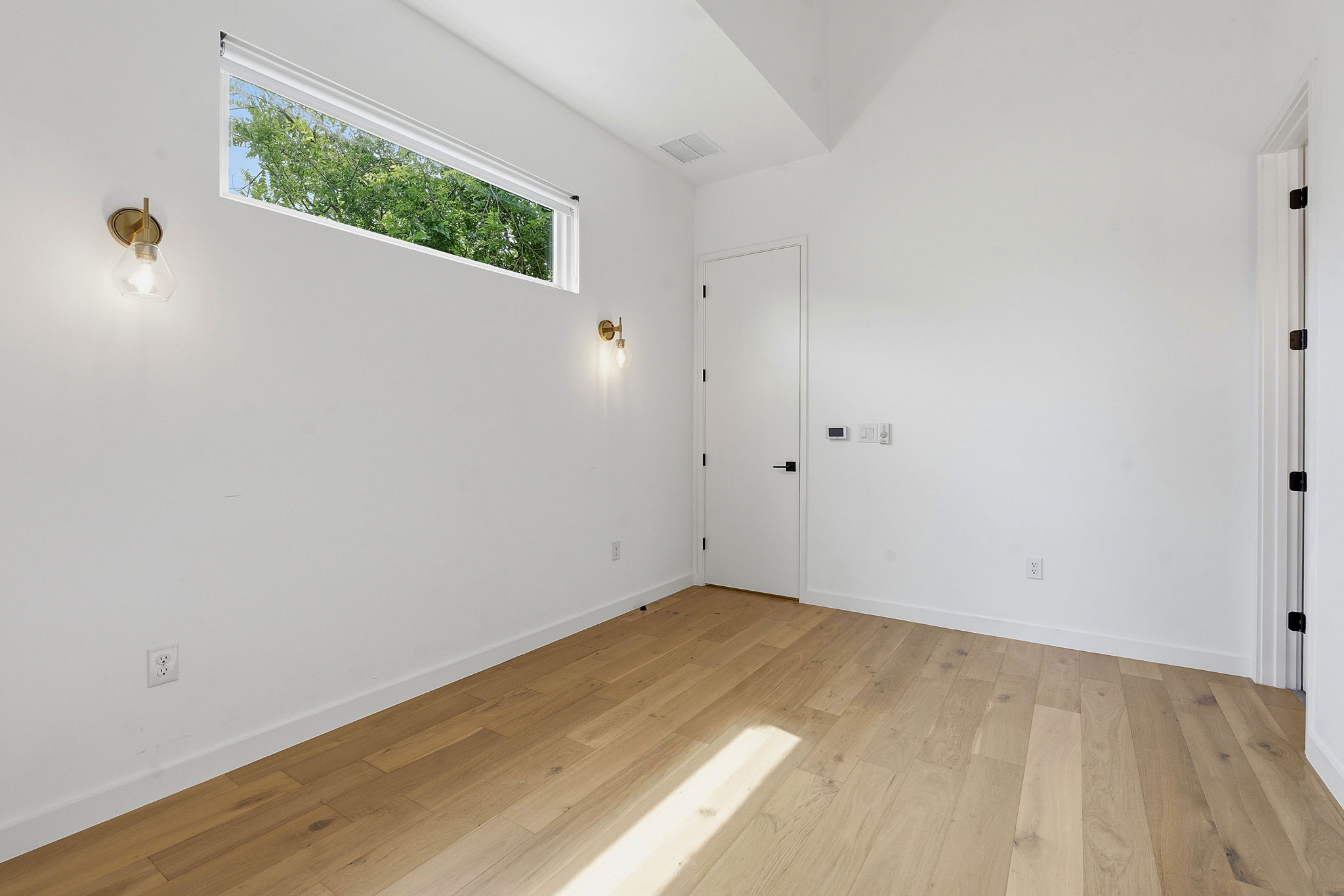 1707 Deloney Street, Unit 2 Austin, TX 78721 - Photo 15 of 26 Natural light illuminates this cozy bedroom with light wood flooring and modern wall sconces.