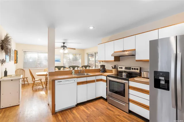 a kitchen with stainless steel appliances a stove a sink a refrigerator a stove and white cabinets with wooden floor